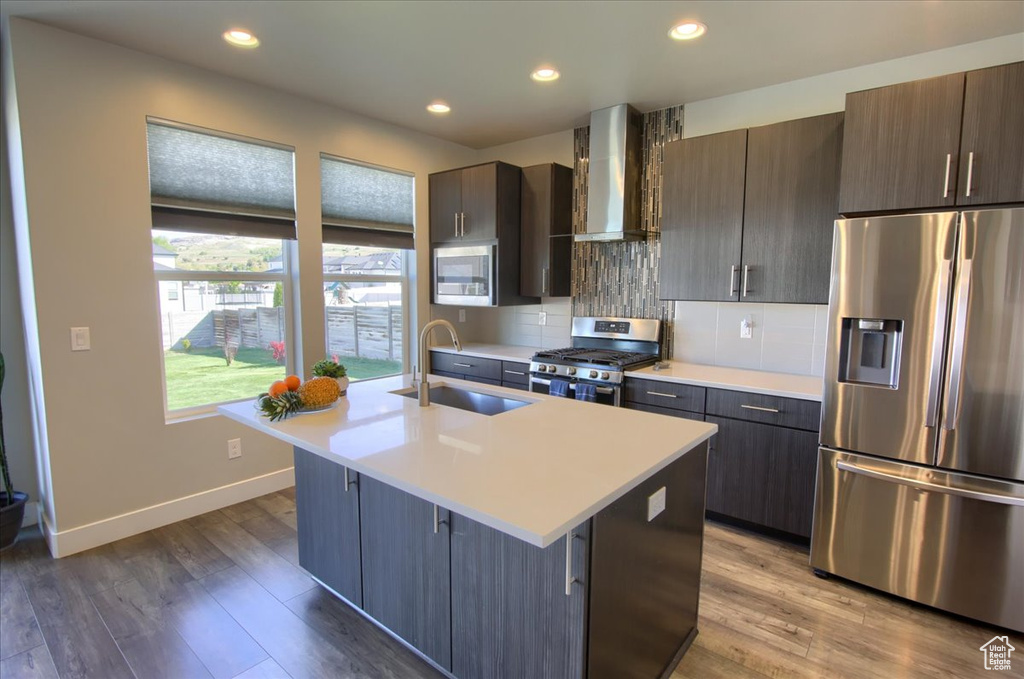 Kitchen featuring wall chimney range hood, appliances with stainless steel finishes, a sink, baseboards, and light countertops