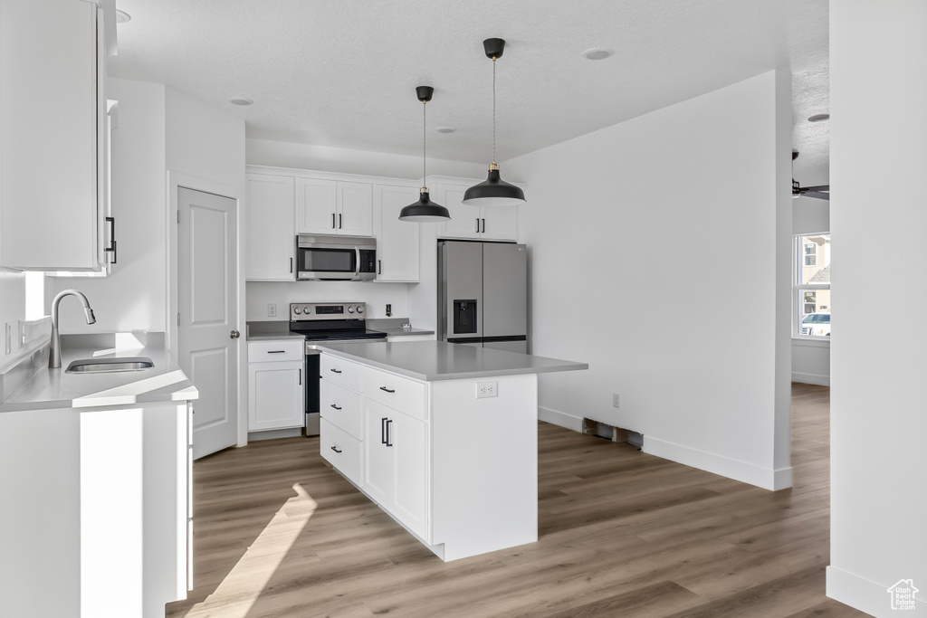 Kitchen with white cabinets, a sink, appliances with stainless steel finishes, a center island, and light wood-type flooring