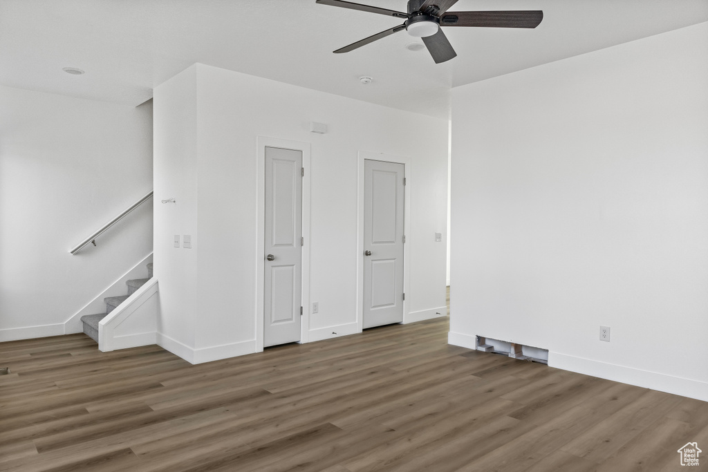 Empty room with a ceiling fan, stairway, wood finished floors, and baseboards