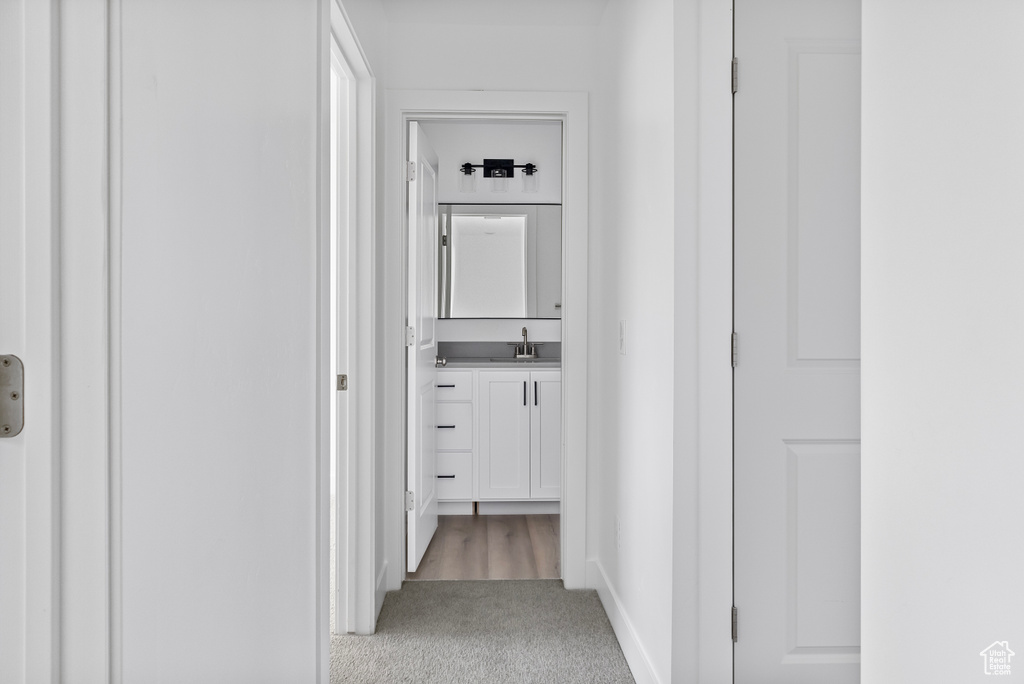 Corridor with baseboards, light colored carpet, and a sink