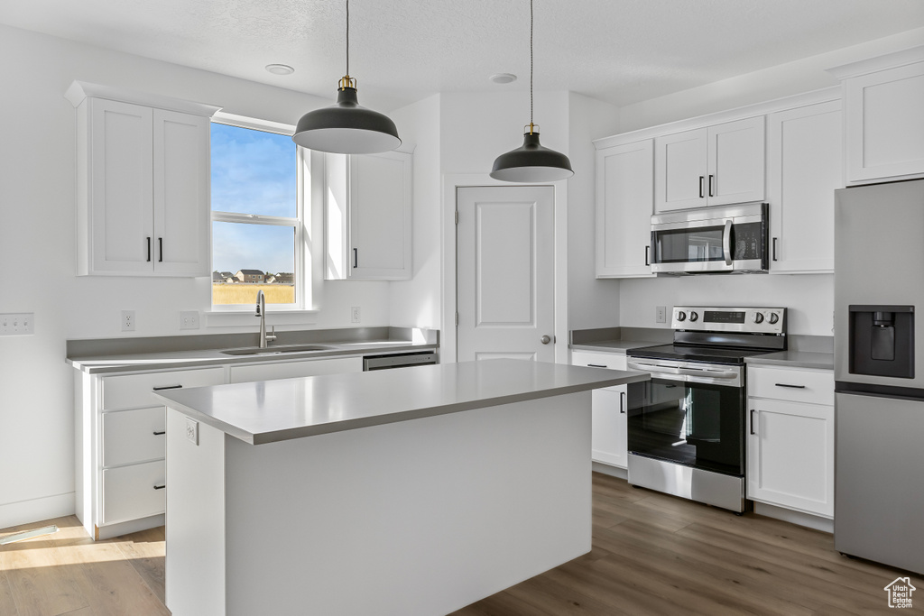 Kitchen with appliances with stainless steel finishes, wood finished floors, white cabinetry, and a sink