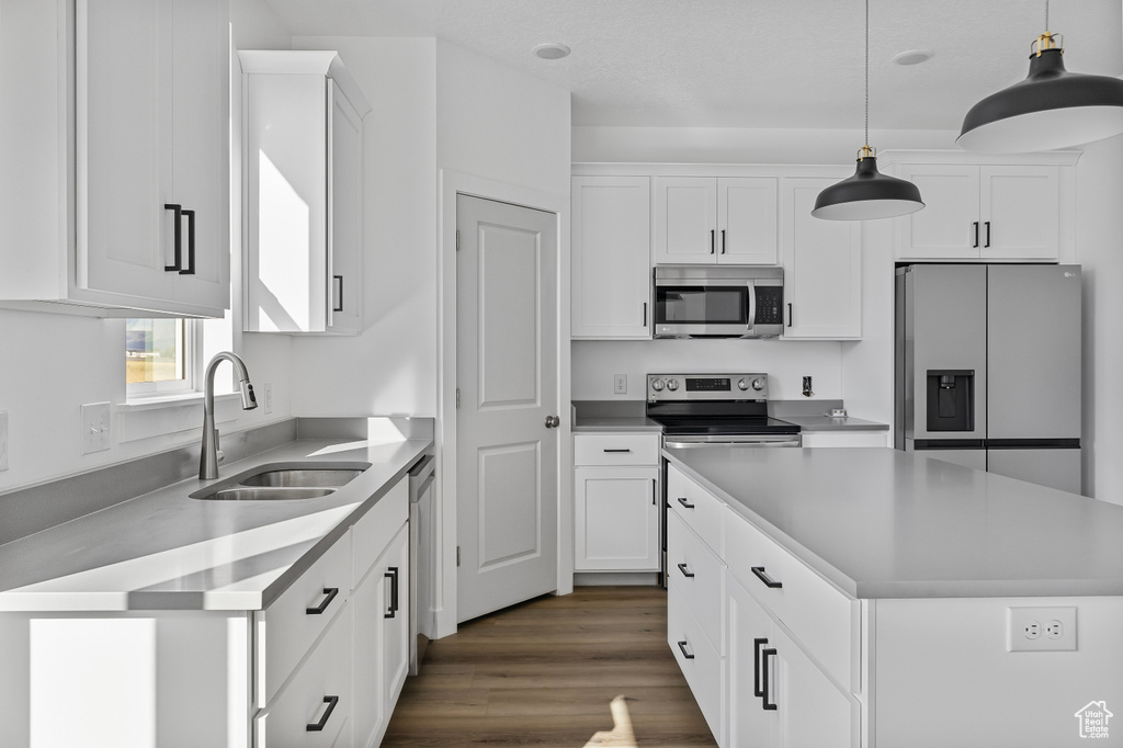 Kitchen featuring decorative light fixtures, a sink, white cabinets, and stainless steel appliances