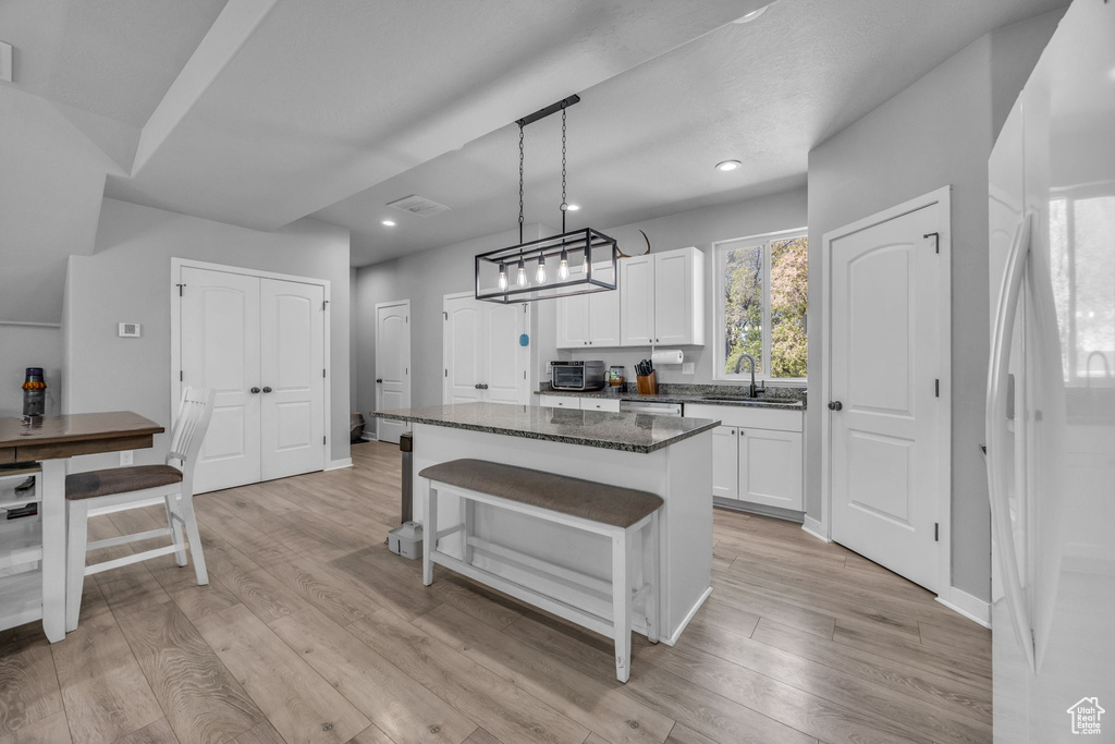 Kitchen featuring a center island, a sink, white cabinets, freestanding refrigerator, and dark stone countertops