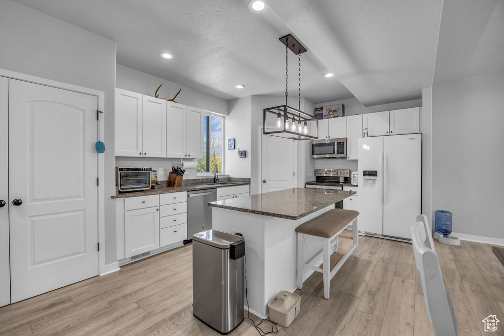 Kitchen featuring a center island, white cabinetry, a sink, light wood finished floors, and stainless steel appliances