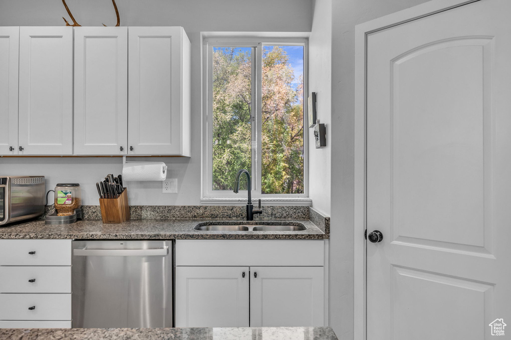 Kitchen featuring stainless steel dishwasher, white cabinets, a sink, and dark stone countertops