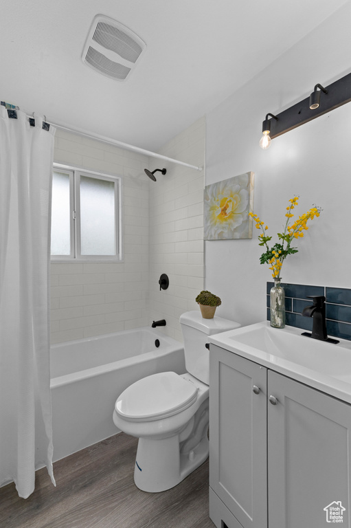Full bath with vanity, toilet, shower / bath combination with curtain, wood finished floors, and visible vents