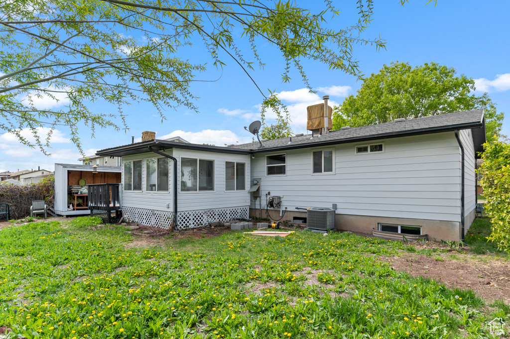 Rear view of house with central air condition unit, a sunroom, a chimney, and a yard