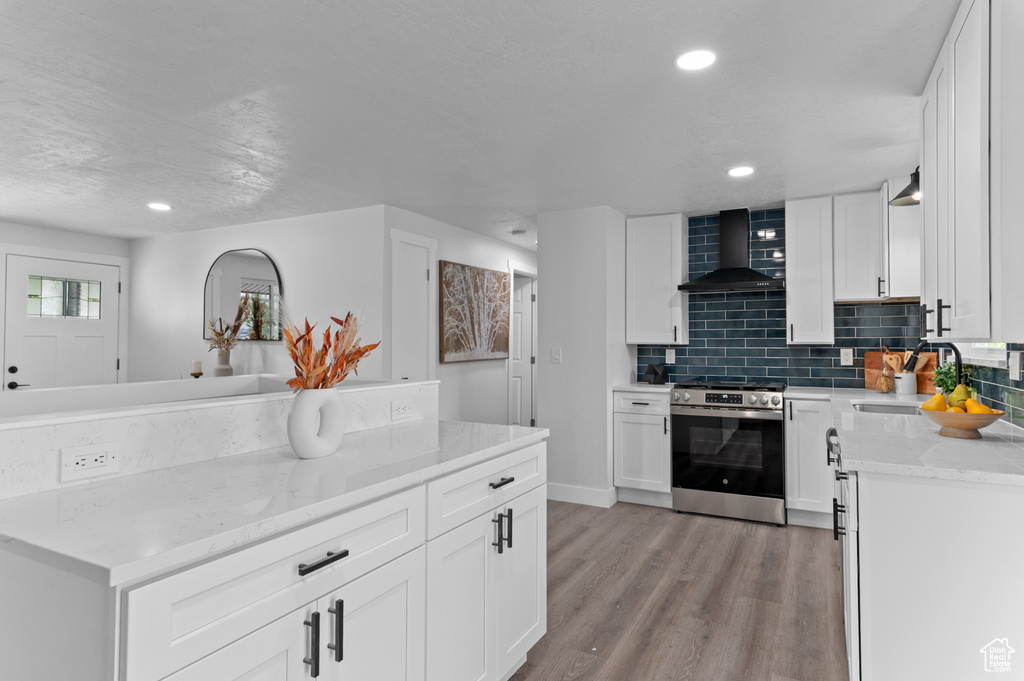 Kitchen featuring wall chimney range hood, backsplash, a sink, light stone counters, and stainless steel electric stove