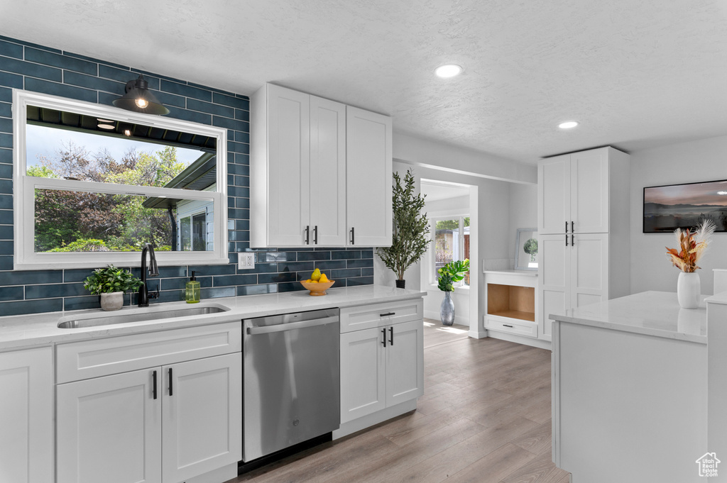 Kitchen with stainless steel dishwasher, a sink, decorative backsplash, and light countertops