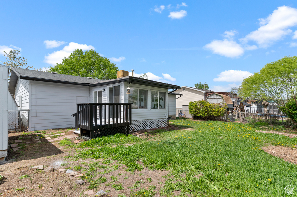 Rear view of house featuring a yard, a deck, fence, and a chimney