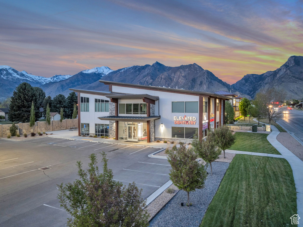 Back of house at dusk with uncovered parking, fence, stone siding, stucco siding, and a mountain view