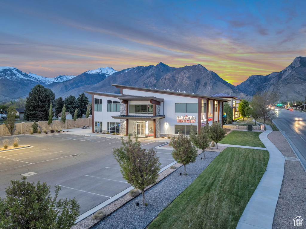 Back of house at dusk with uncovered parking, fence, stone siding, stucco siding, and a mountain view
