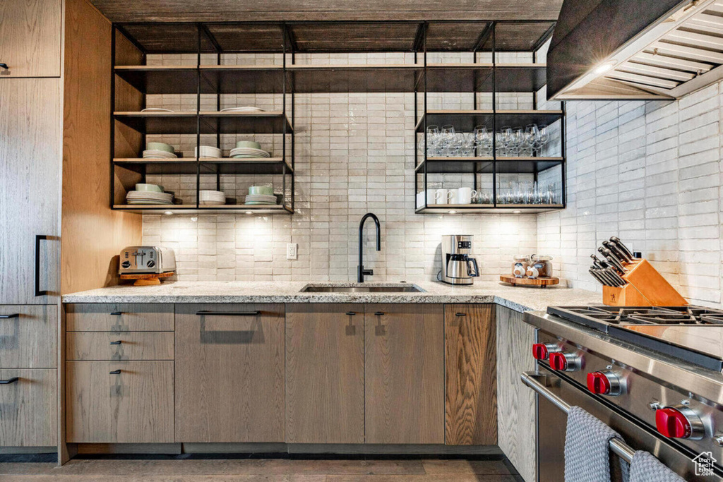 Kitchen with wall chimney range hood, decorative backsplash, high end stainless steel range oven, and a sink