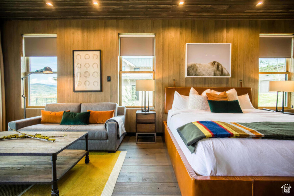 Bedroom with wood-type flooring, recessed lighting, wood walls, and multiple windows