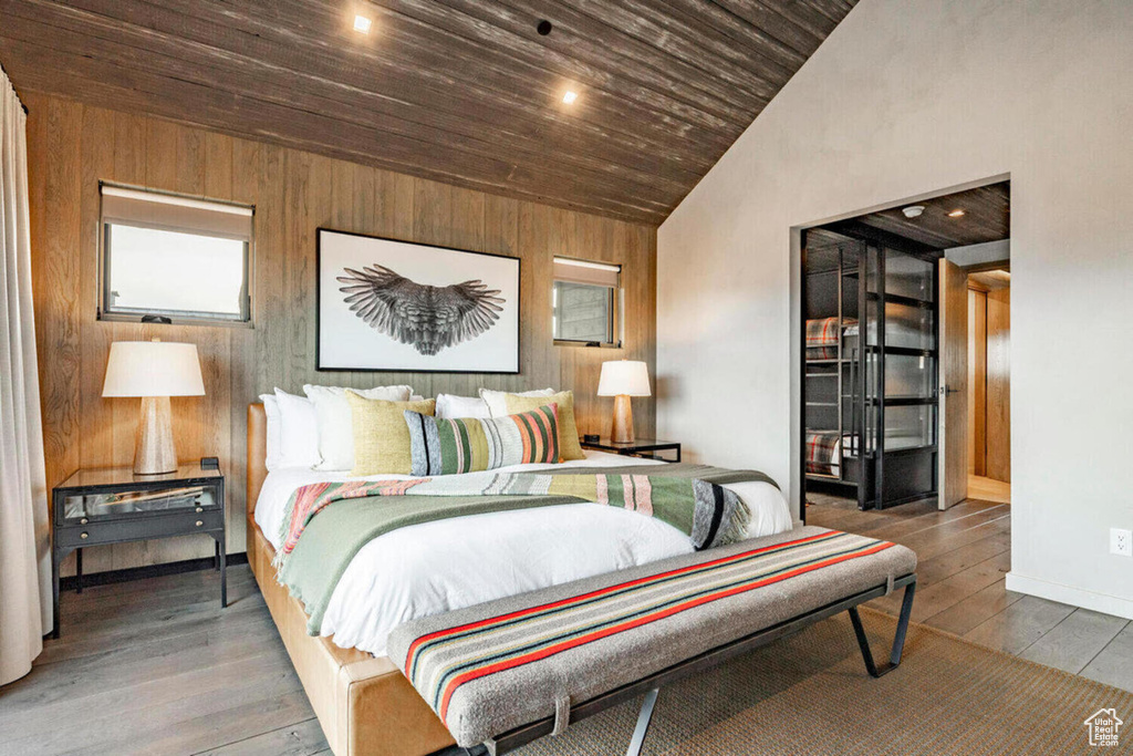 Bedroom featuring wooden walls, high vaulted ceiling, baseboards, wooden ceiling, and wood finished floors