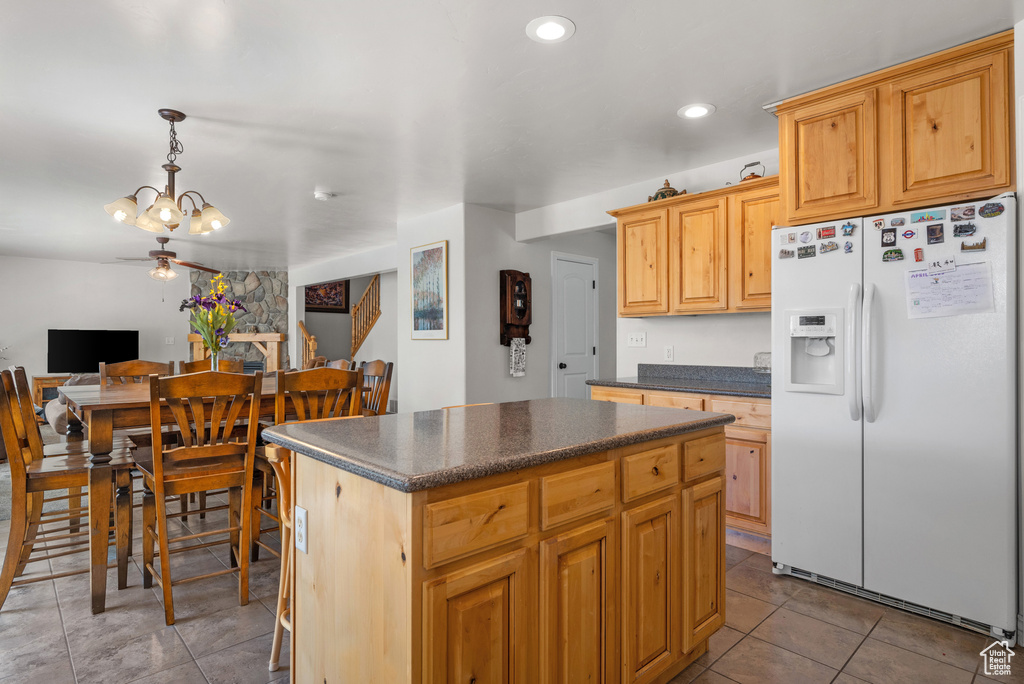 Kitchen with a kitchen island, dark countertops, light tile patterned floors, a notable chandelier, and white fridge with ice dispenser
