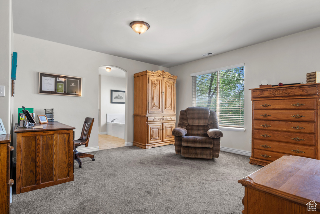 Home office with arched walkways, baseboards, light carpet, and visible vents