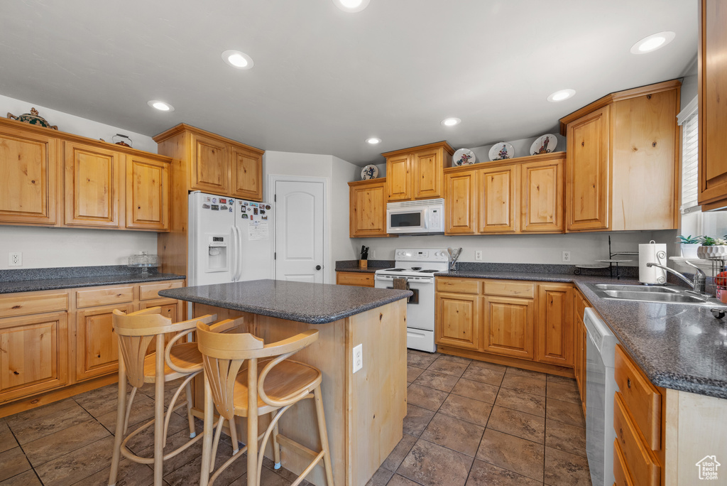 Kitchen featuring a breakfast bar area, dark countertops, a center island, a sink, and white appliances