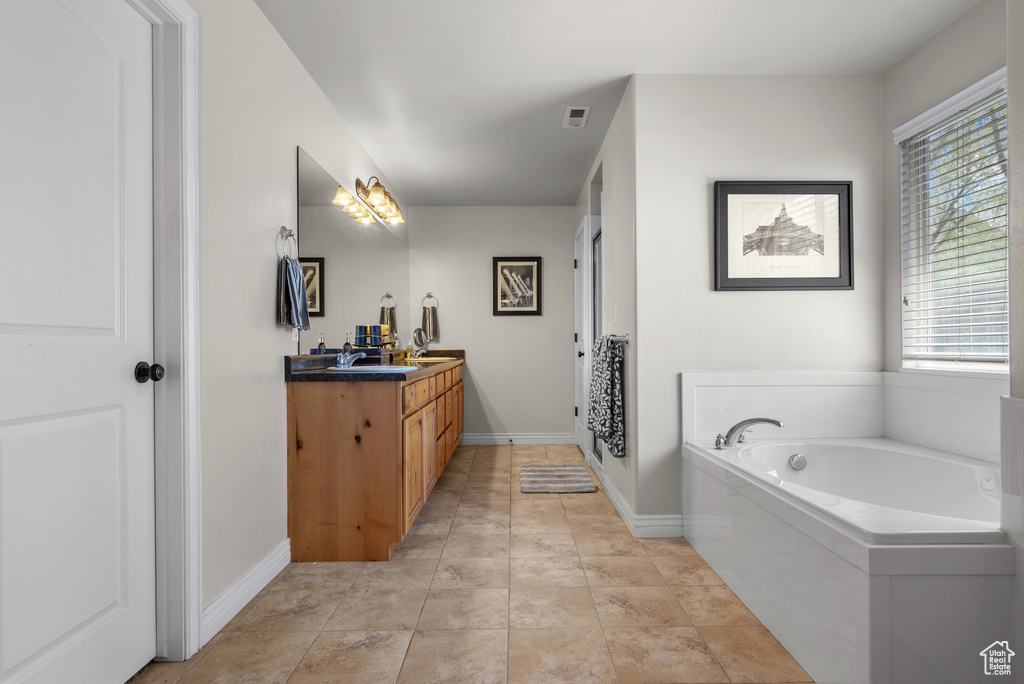Bathroom with double vanity, baseboards, visible vents, and a bath