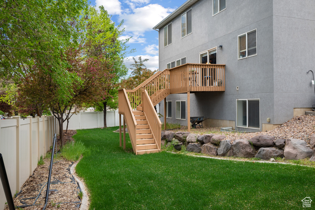 Back of house with a wooden deck, a fenced backyard, stucco siding, stairs, and a lawn
