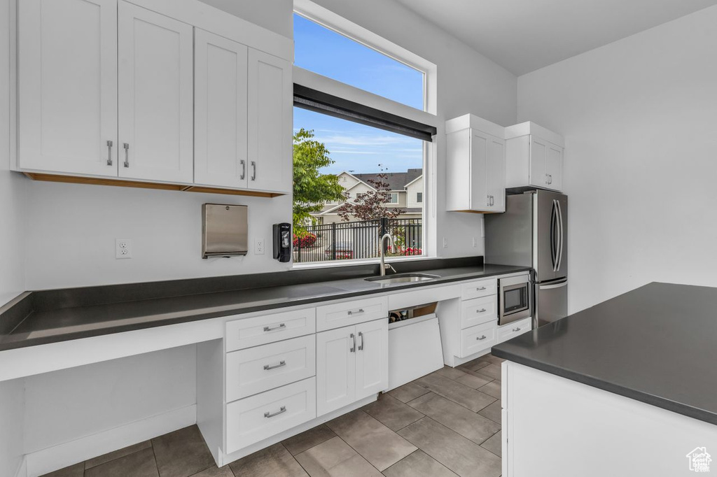 Kitchen with a sink, appliances with stainless steel finishes, white cabinets, and dark countertops