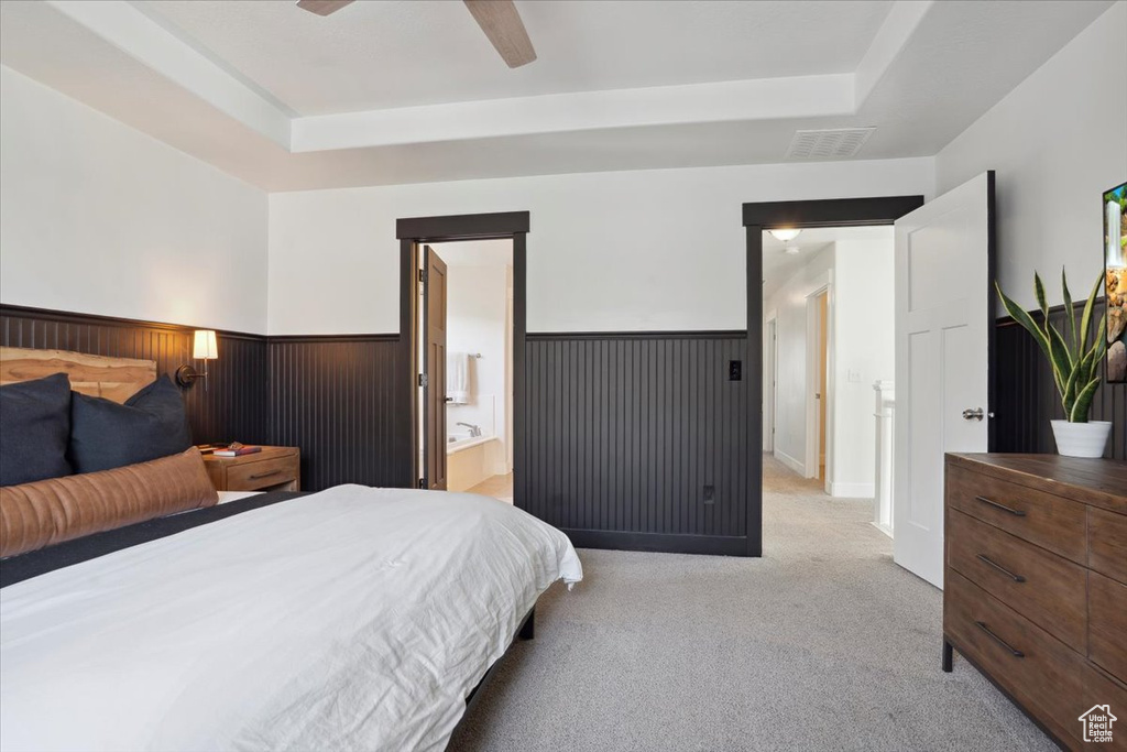Bedroom featuring light colored carpet, wainscoting, a ceiling fan, a tray ceiling, and visible vents
