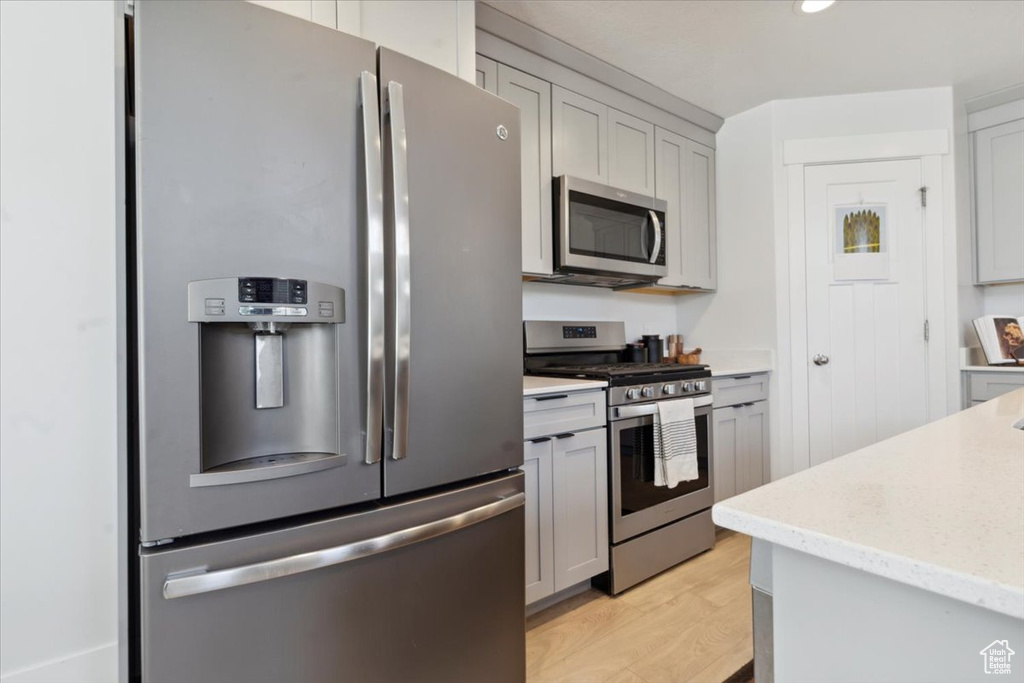 Kitchen featuring stainless steel appliances, light stone countertops, gray cabinetry, and light wood finished floors