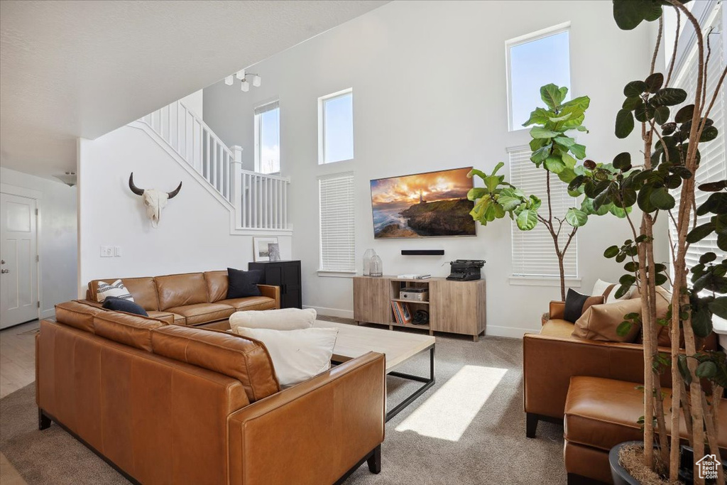Carpeted living area with baseboards, a high ceiling, stairs, and a wealth of natural light