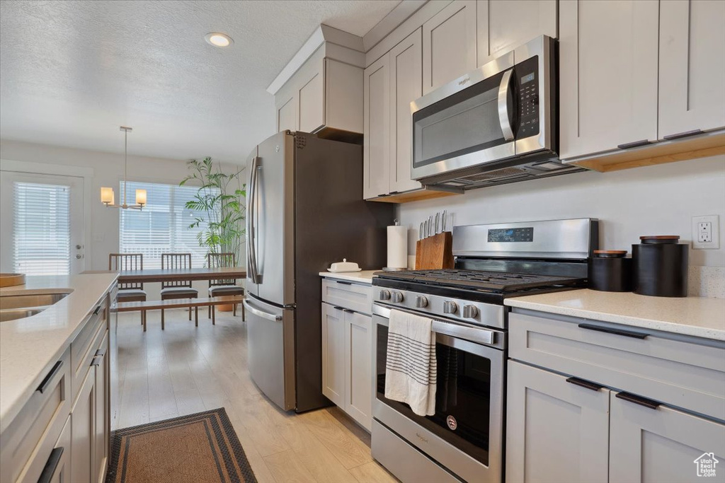 Kitchen with hanging light fixtures, a notable chandelier, appliances with stainless steel finishes, light wood finished floors, and recessed lighting
