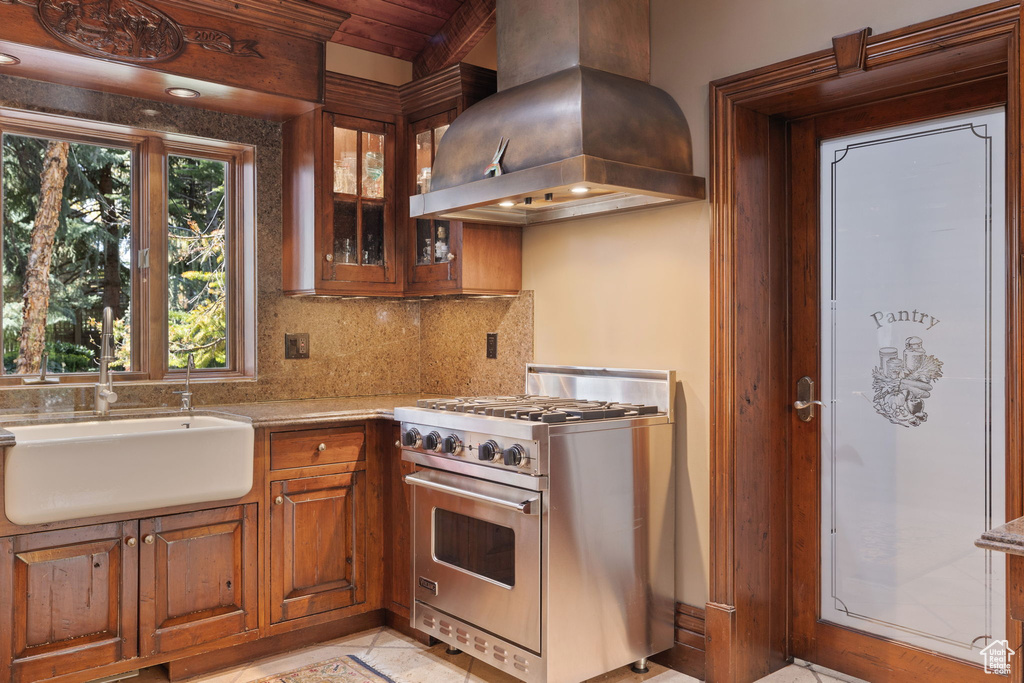 Kitchen featuring brown cabinetry, high end stainless steel range, island range hood, tasteful backsplash, and a sink