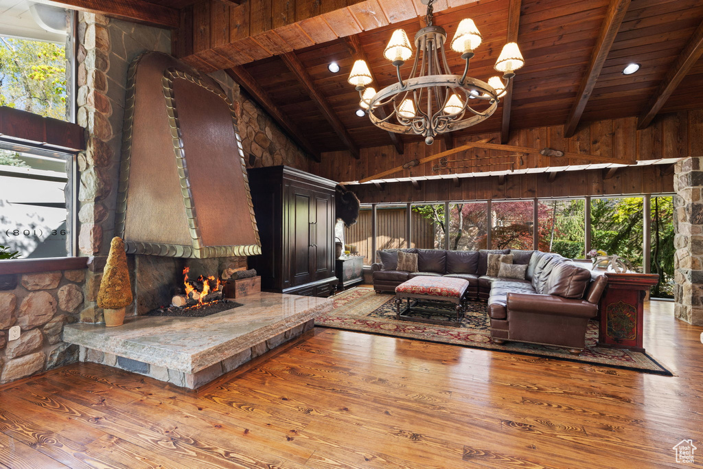 Living room featuring a notable chandelier, lofted ceiling with beams, a stone fireplace, hardwood / wood-style floors, and wood ceiling