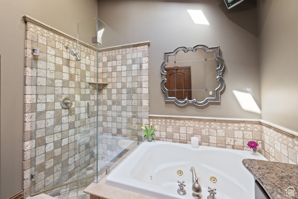 Full bath featuring a whirlpool tub, tiled shower, and a wainscoted wall