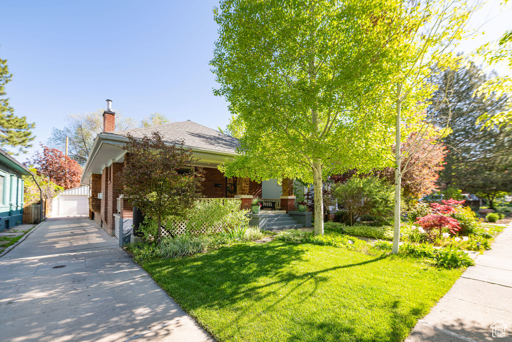 View of front of home with brick siding, a porch, a front yard, a chimney, and an outdoor structure