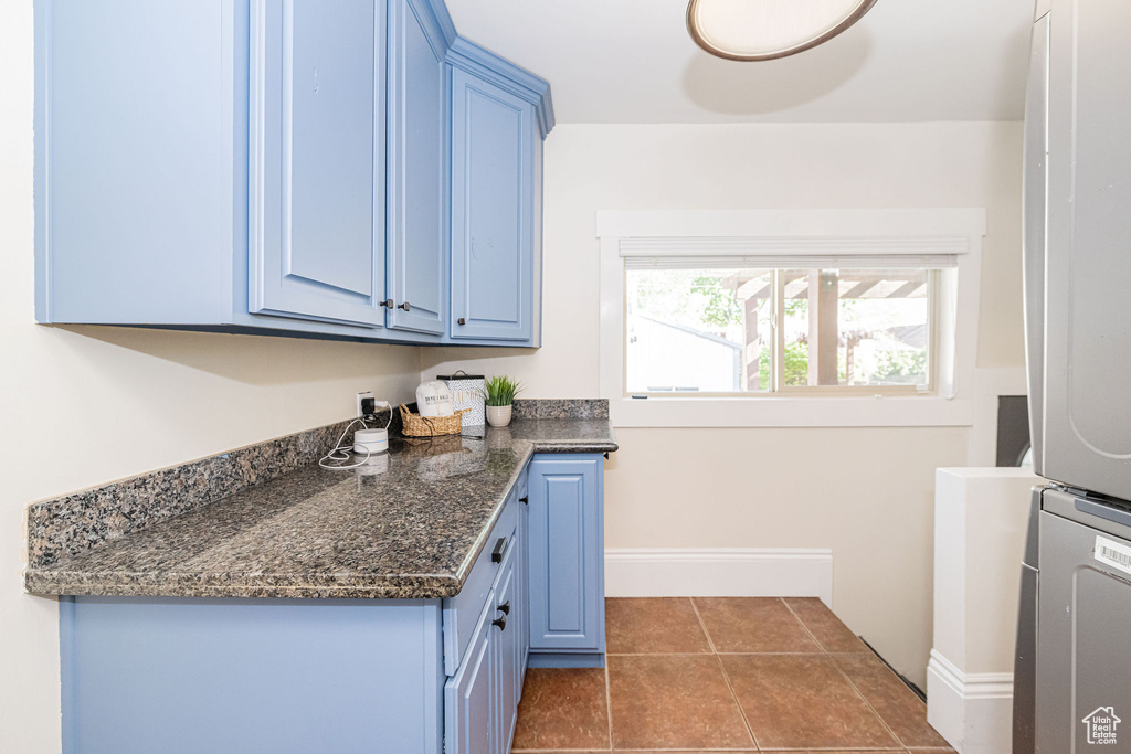 Clothes washing area with cabinet space, dark tile patterned floors, baseboards, and stacked washer / dryer