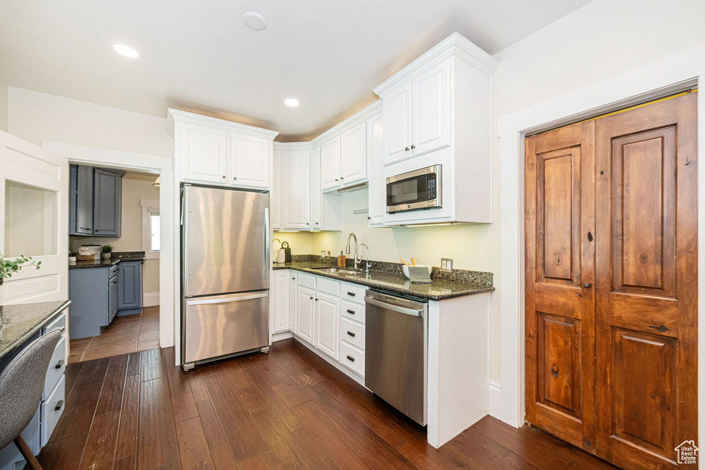 Kitchen with dark wood-style flooring, stainless steel appliances, white cabinets, and a sink