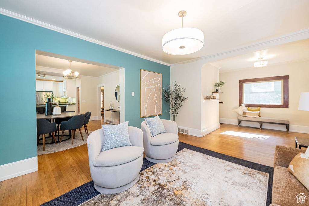 Living room featuring arched walkways, visible vents, ornamental molding, and light wood-style floors
