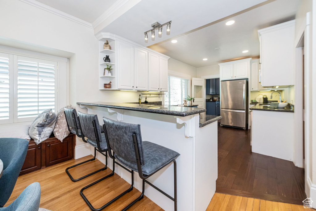 Kitchen with a kitchen bar, open shelves, freestanding refrigerator, a peninsula, and white cabinetry