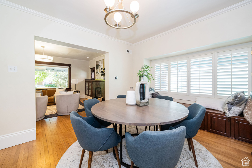 Dining area featuring an inviting chandelier, a fireplace, baseboards, light wood-type flooring, and ornamental molding