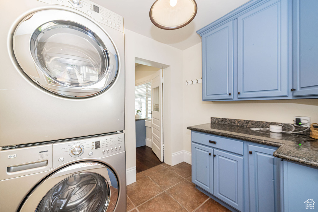 Clothes washing area featuring cabinet space, dark tile patterned floors, baseboards, and stacked washing maching and dryer