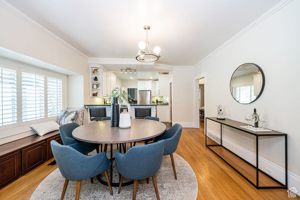 Dining space featuring a wealth of natural light, ornamental molding, light wood-style flooring, and a chandelier