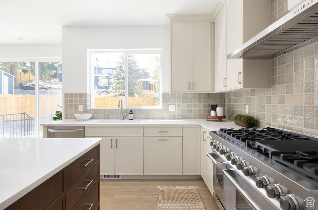 Kitchen with wall chimney range hood, light wood-type flooring, light countertops, a sink, and appliances with stainless steel finishes