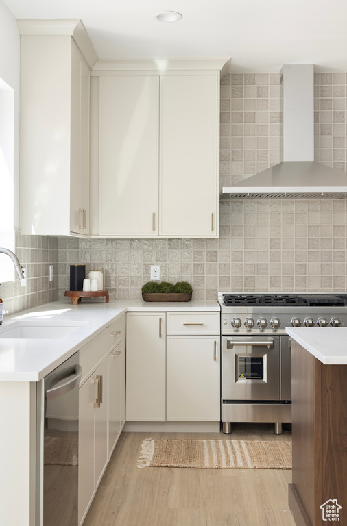 Kitchen with stainless steel appliances, light wood finished floors, a sink, and wall chimney exhaust hood