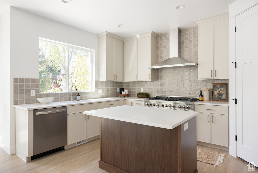 Kitchen with light countertops, wall chimney exhaust hood, a sink, light wood-style flooring, and dishwasher