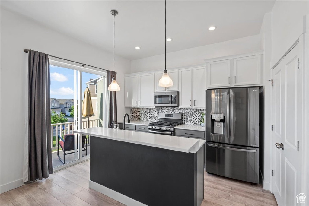Kitchen featuring stainless steel appliances, backsplash, light countertops, white cabinets, and light wood finished floors