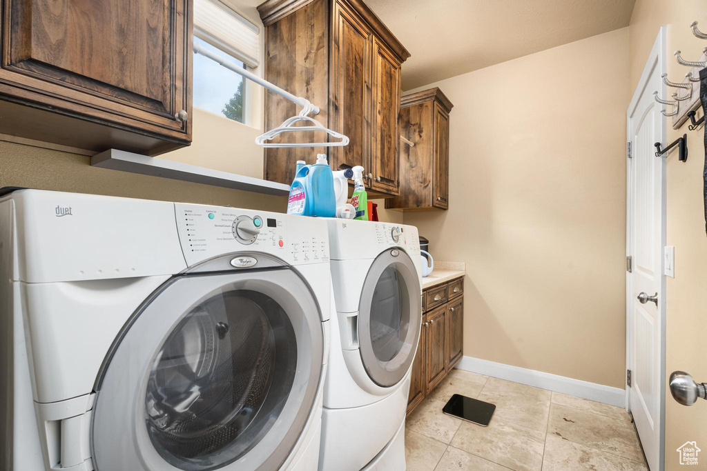Laundry area featuring cabinet space, light tile patterned flooring, baseboards, and washing machine and dryer