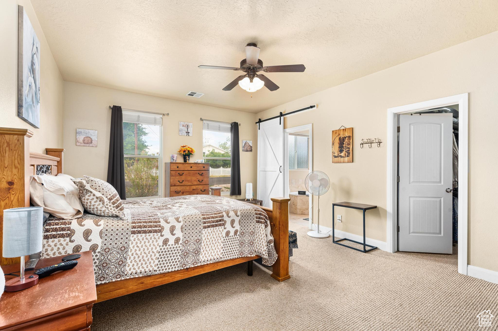 Bedroom with ceiling fan, light colored carpet, a barn door, baseboards, and visible vents
