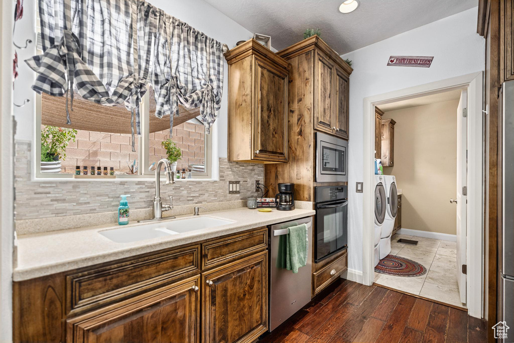 Kitchen featuring washing machine and clothes dryer, appliances with stainless steel finishes, a sink, light countertops, and dark wood-type flooring