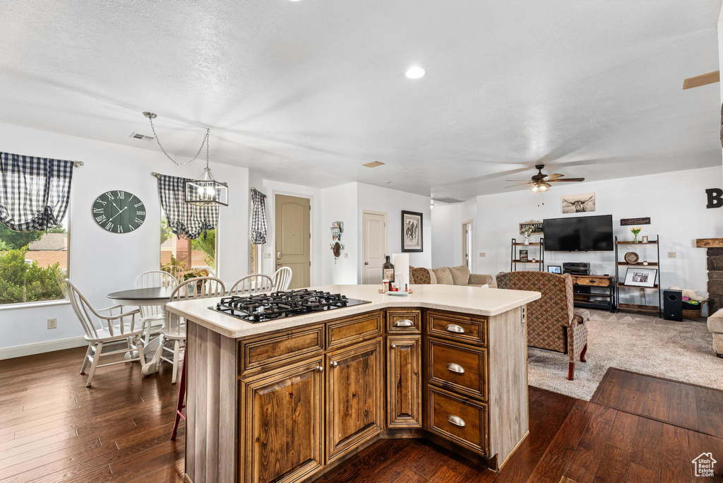 Kitchen featuring dark wood-style flooring, light countertops, ceiling fan with notable chandelier, a center island, and gas stovetop