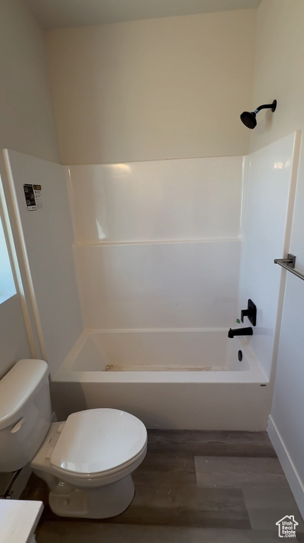 Bathroom with baseboards, toilet, wood finished floors, and  shower combination