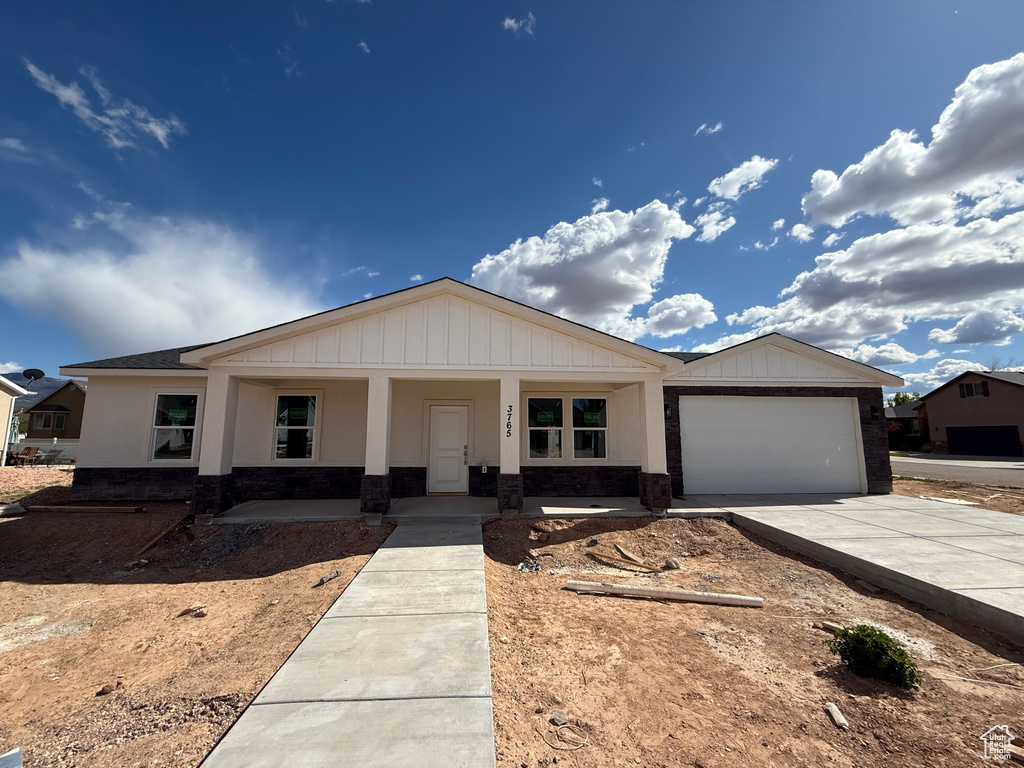 Single story home featuring a porch, an attached garage, stone siding, and concrete driveway